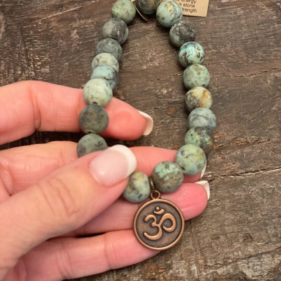 Hand holding a Turquoise Bracelet featuring 10mm matte African turquoise beads and vintage brass om charm.